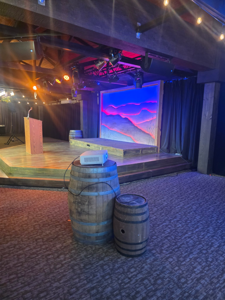 Stage decorated with wooden barrels and a projector sitting on a barrel