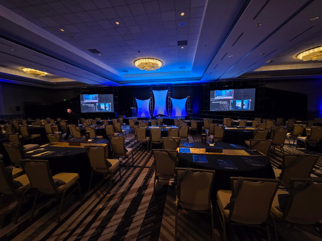 Corporate conference ballroom with blue uplighting and dual screens