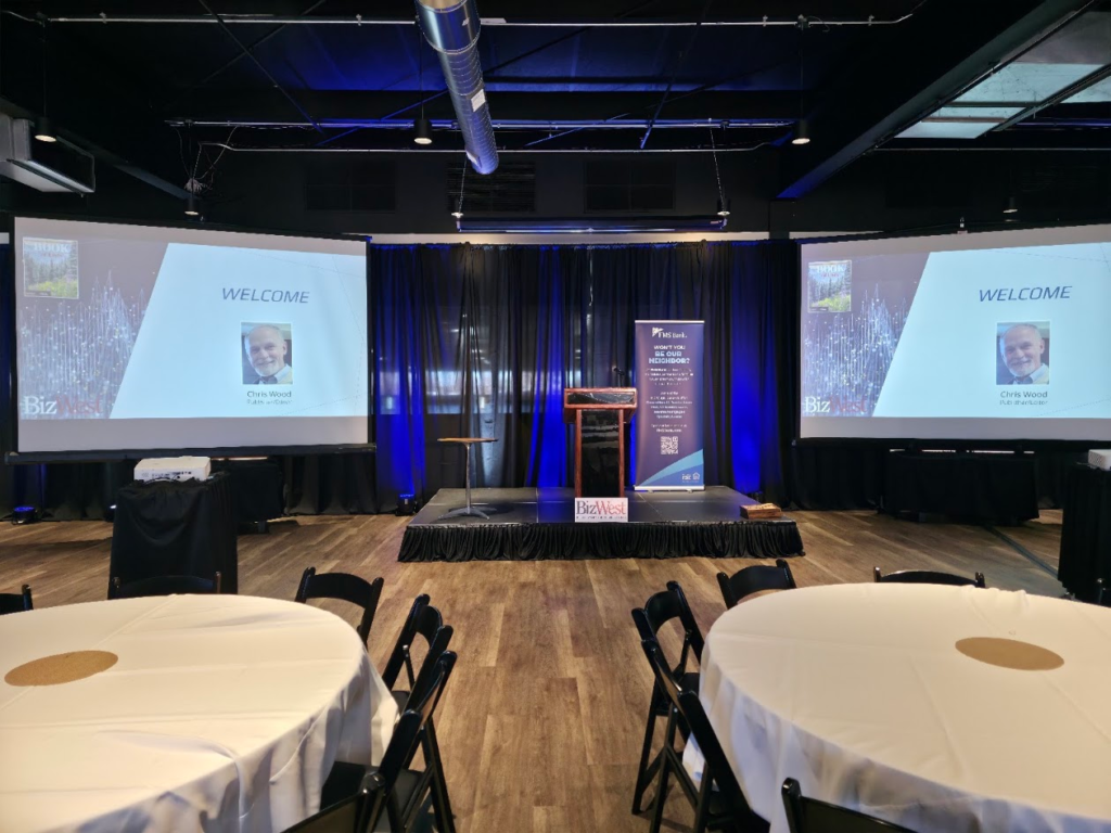 BizWest corporate stage with dual projection screens and blue uplighting