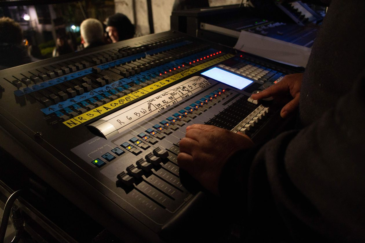 Lighting technician's hands on a concert lighting console with labeled faders