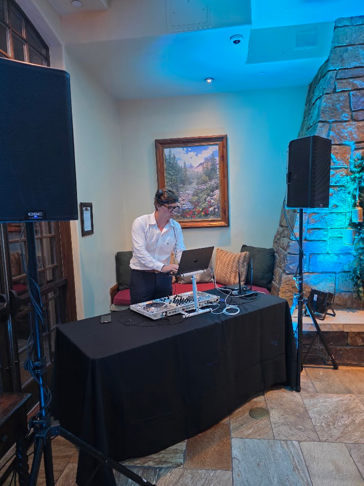 DJ with laptop and controller between two QSC speakers and blue uplighting
