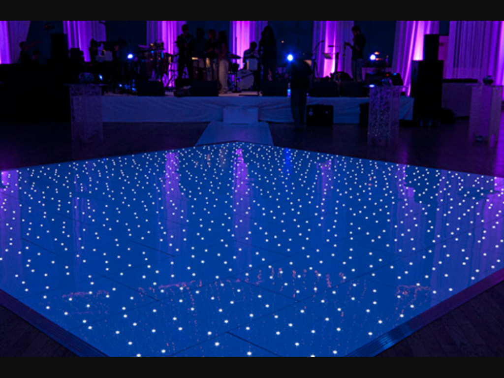 Blue starlit LED dance floor glowing in front of a band stage with purple uplighting at a wedding reception