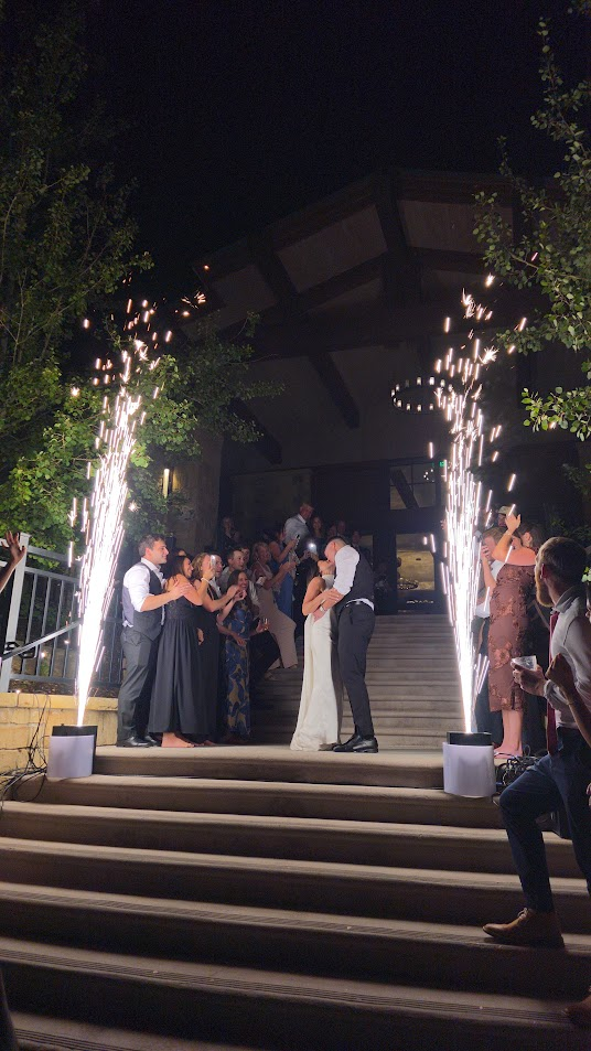 Bride and groom kissing on outdoor steps between two cold spark fountains during their nighttime wedding send-off