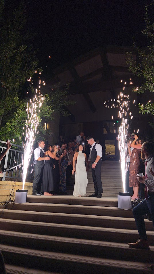 Bride and groom holding hands on venue steps between two cold spark fountains at their grand exit